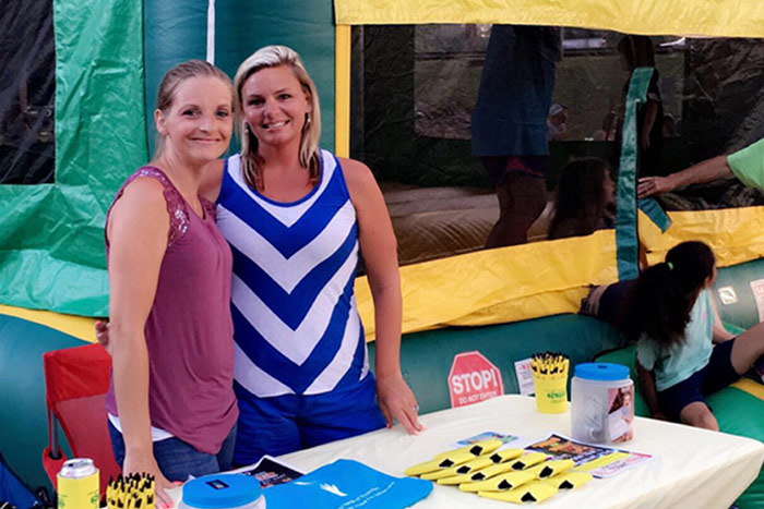 two women volunteer at table in front of bounce house